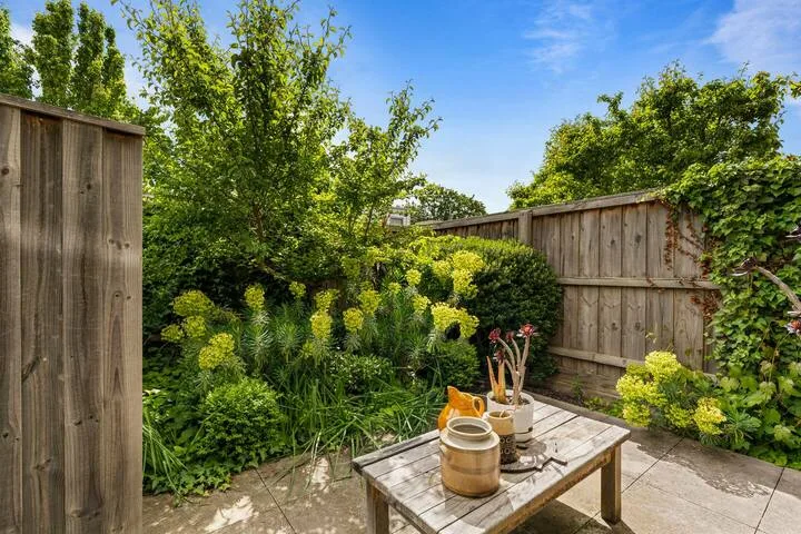 A garden patio with a wooden table surrounded by lush greenery.