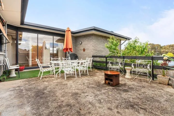 A paved outdoor patio has a dining table, seating, and an orange umbrella.