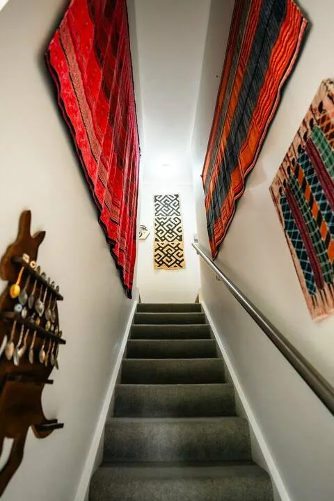 A narrow staircase with dark steps and colorful woven textiles on the walls.