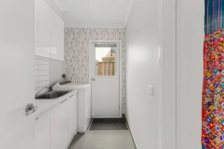 A narrow laundry room with white cabinets, a sink, and a washing machine.