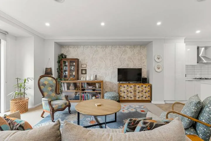A bright living room with patterned wallpaper, a television, and seating around a coffee table.