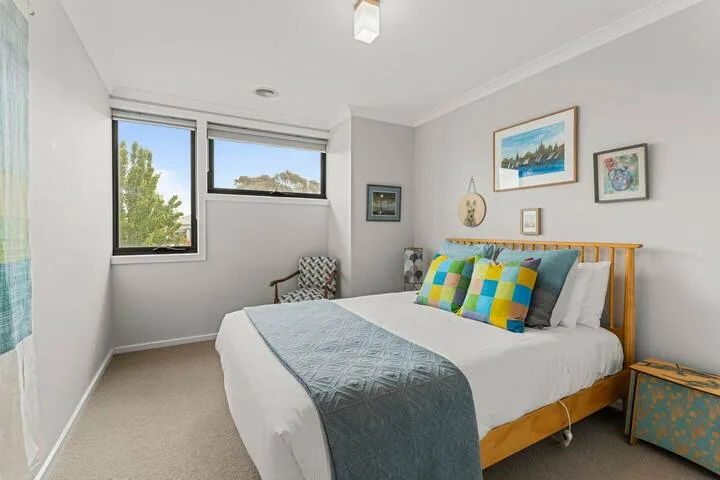 A bedroom with a bed, colorful cushions, and windows overlooking greenery.