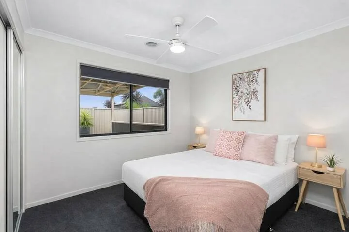 A bedroom with a bed dressed in white and pink bedding.