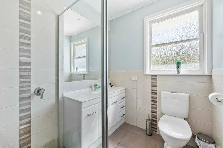 A bright bathroom with a glass shower, vanity, and toilet.