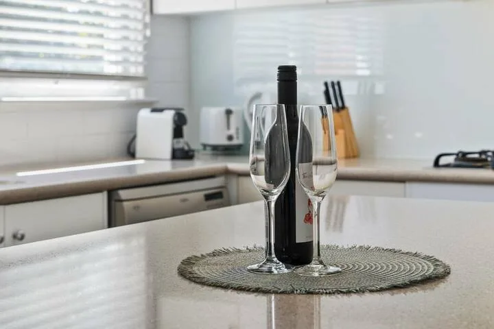 A bright kitchen counter holds a bottle of wine and two glasses.