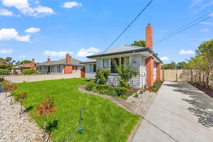 A small house stands beside a paved driveway and a green lawn.