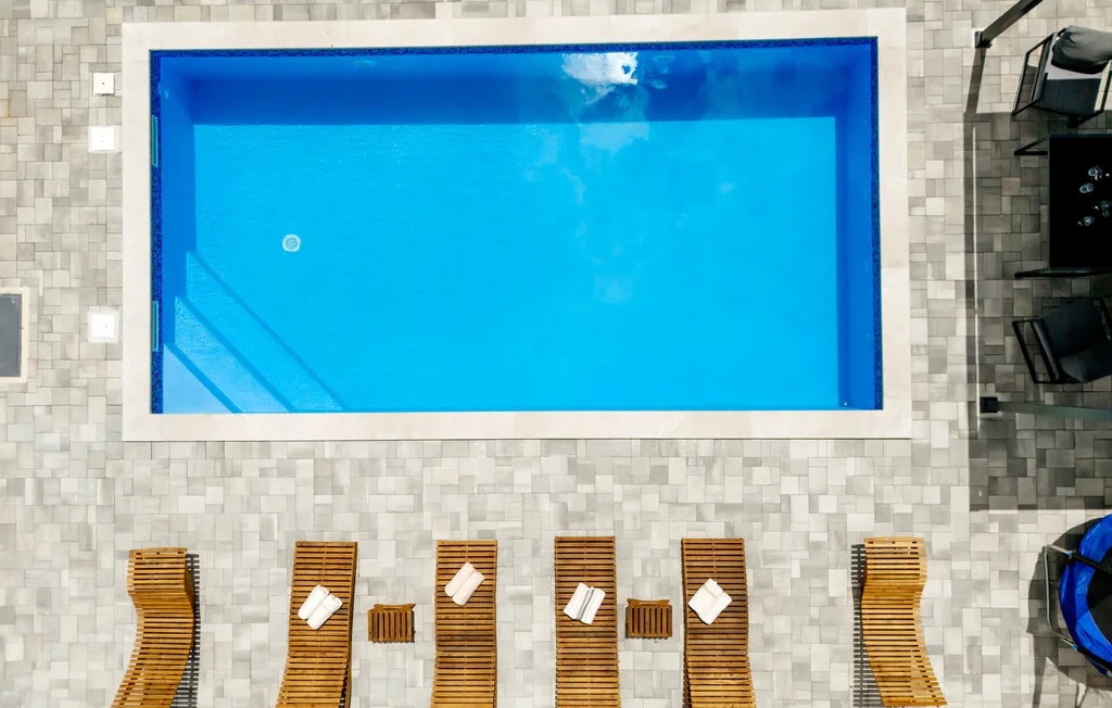 Una piscina al aire libre está junto a filas de tumbonas sobre una terraza pavimentada.