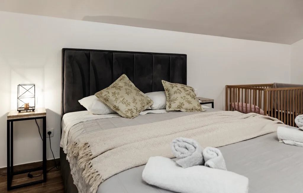 Un dormitorio con una cama tendida, cojines estampados y toallas dobladas.