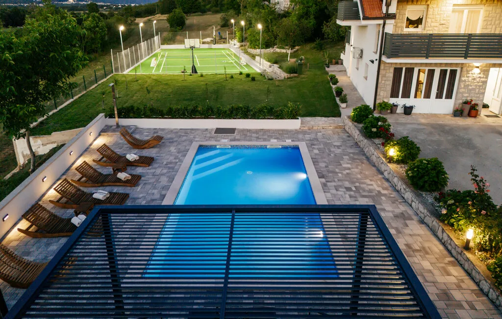 Una piscina exterior y un patio pavimentado dan a una cancha deportiva cercada.
