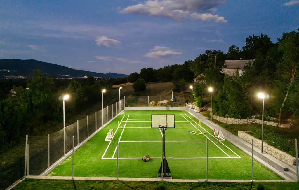 Una cancha de baloncesto al aire libre está iluminada bajo el cielo del atardecer.