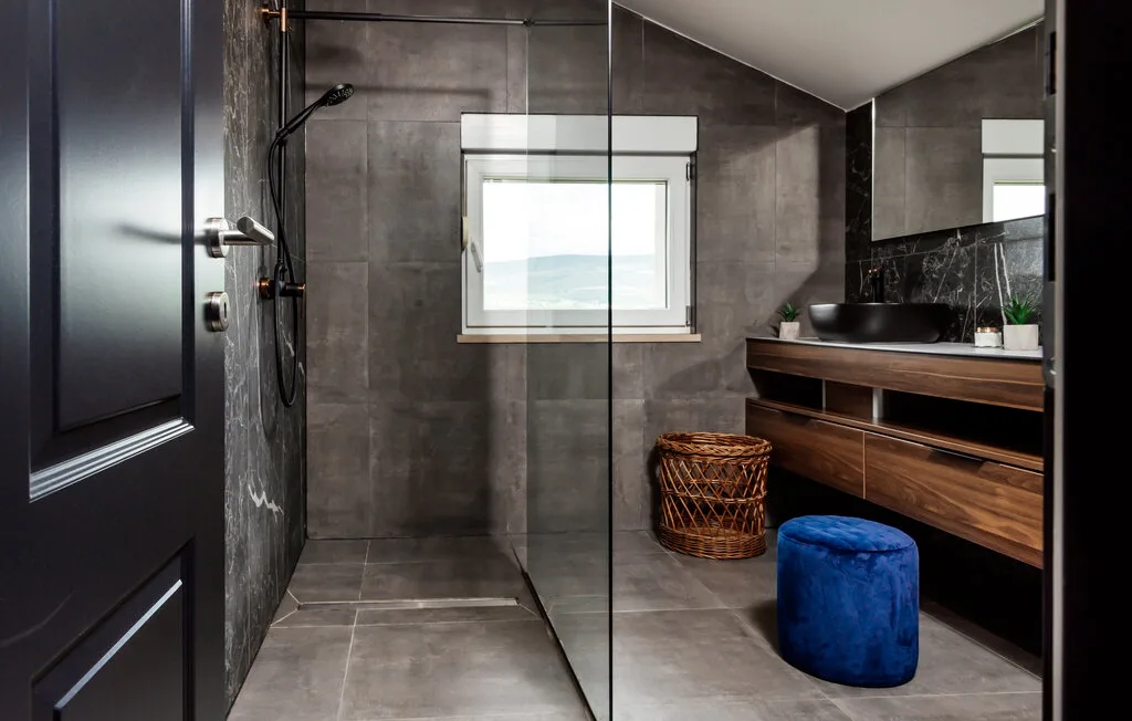 Un baño moderno con ducha de vidrio, paredes oscuras y un mueble de madera.