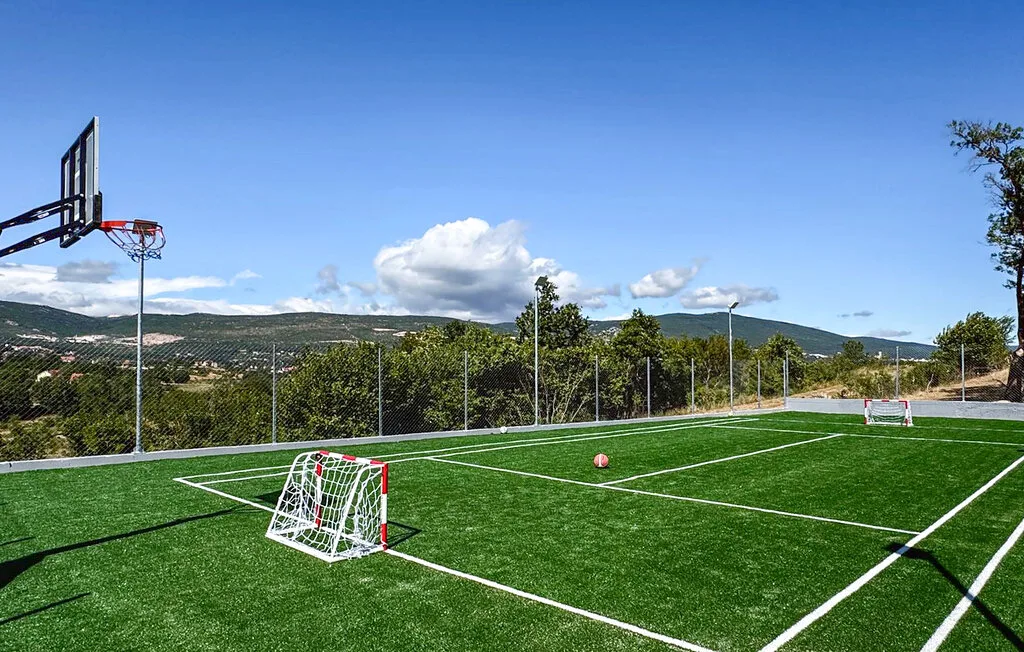 Una cancha deportiva al aire libre tiene césped artificial, porterías y una canasta de baloncesto.