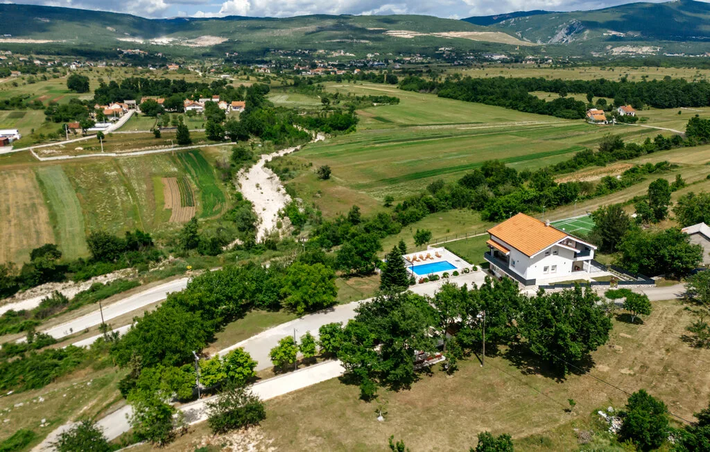 Vista aérea de una casa y una piscina junto a campos verdes y colinas lejanas.