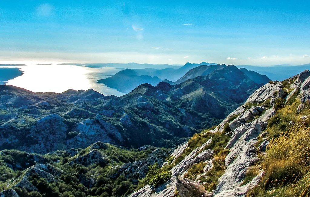 Paisaje montañoso con vistas a una costa iluminada bajo un cielo azul despejado.