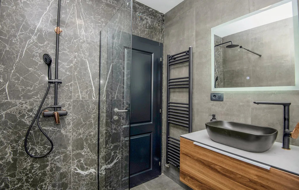 Un baño moderno con ducha de vidrio, puerta oscura y tocador de madera.