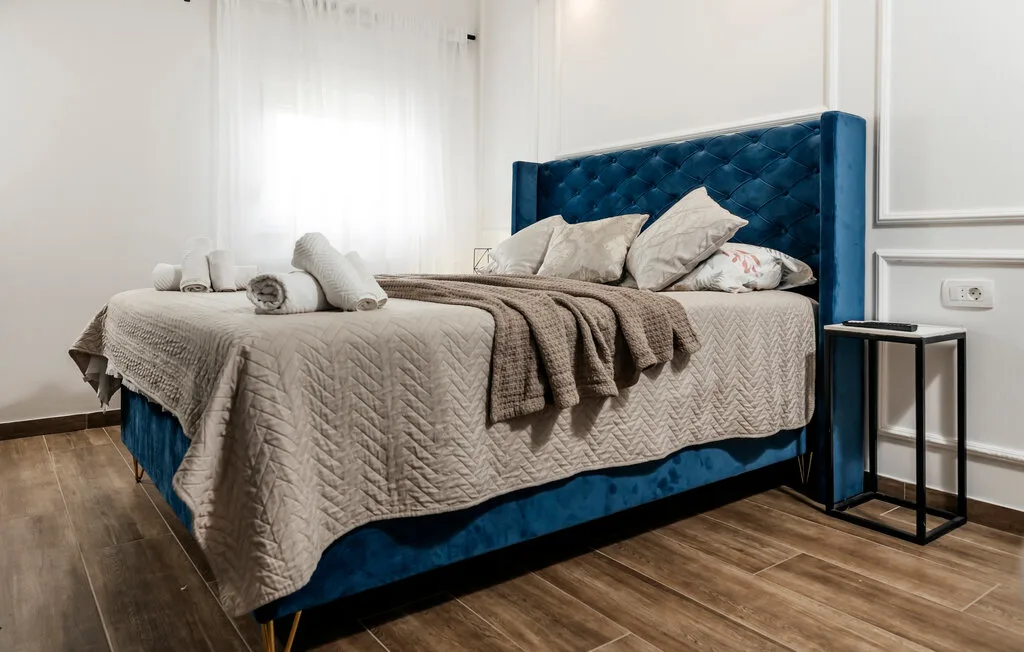 Dormitorio con una cama bien hecha y un cabecero tapizado azul.