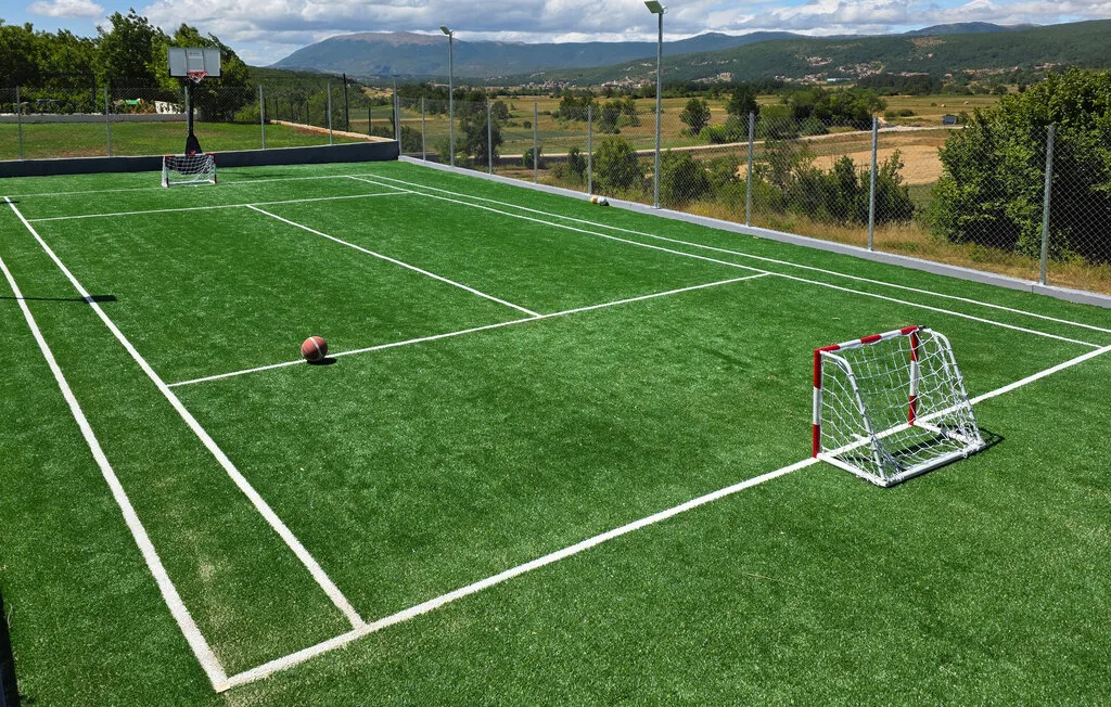 Una cancha deportiva al aire libre de césped artificial, con líneas pintadas, porterías y colinas alrededor.