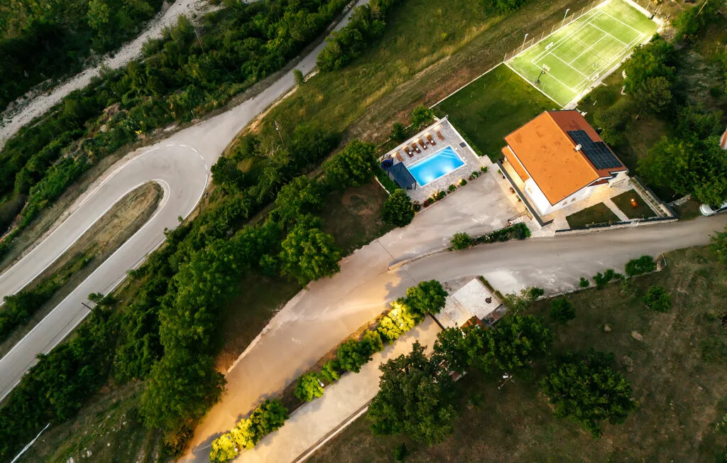 Vista aérea de una propiedad con piscina, un edificio y una cancha deportiva.