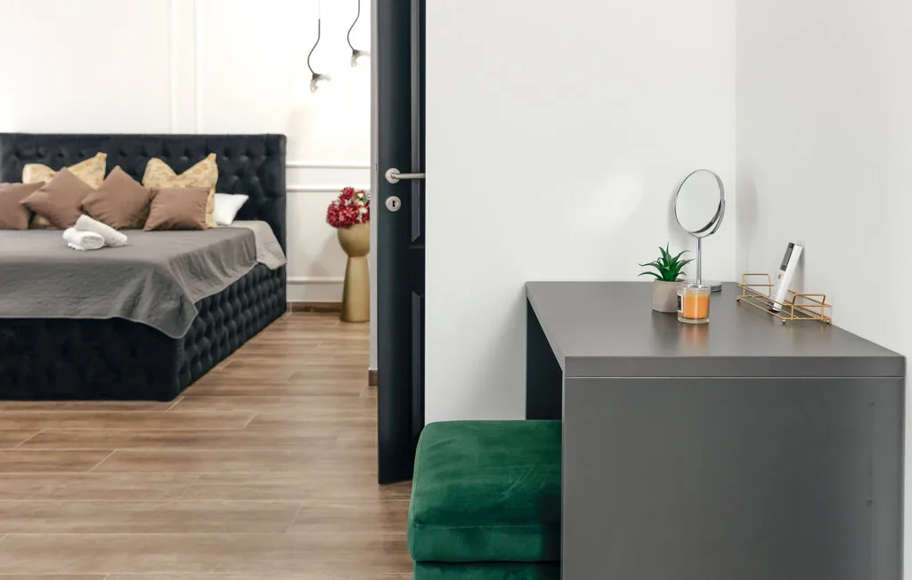 Un dormitorio con una cama oscura junto a un tocador gris y asientos verdes.