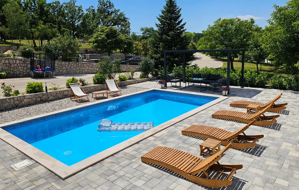 Una piscina al aire libre está rodeada de una terraza pavimentada y asientos para descansar.