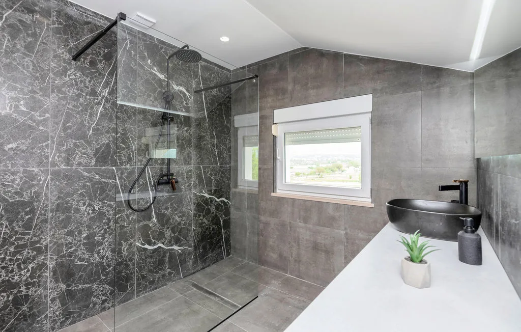 Un baño moderno con ducha de cristal, una ventana y un lavabo sobre encimera.