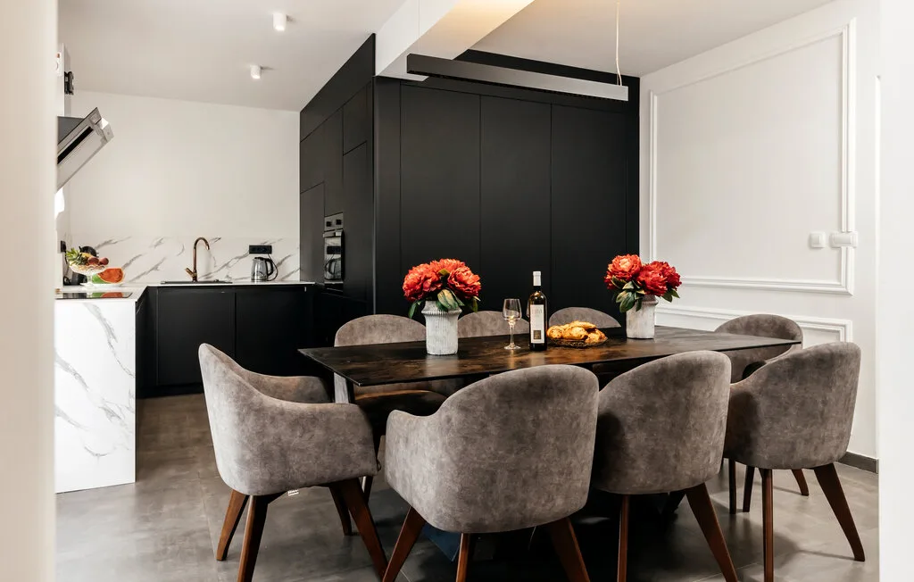 Comedor con una mesa oscura y asientos tapizados junto a una cocina.