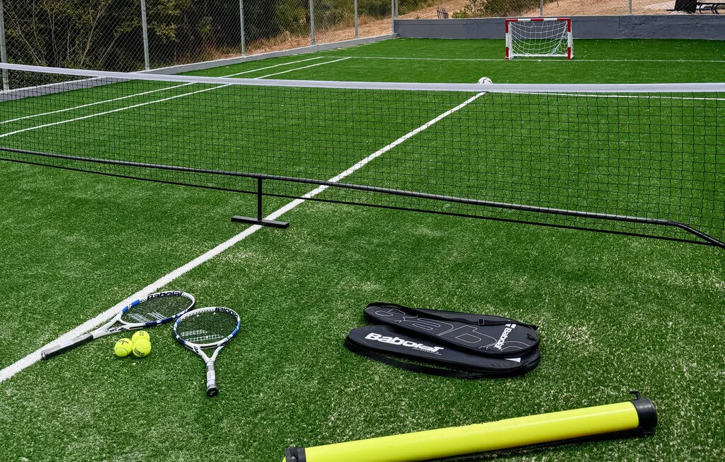 Una cancha deportiva exterior cercada, con raquetas y pelotas sobre césped artificial.