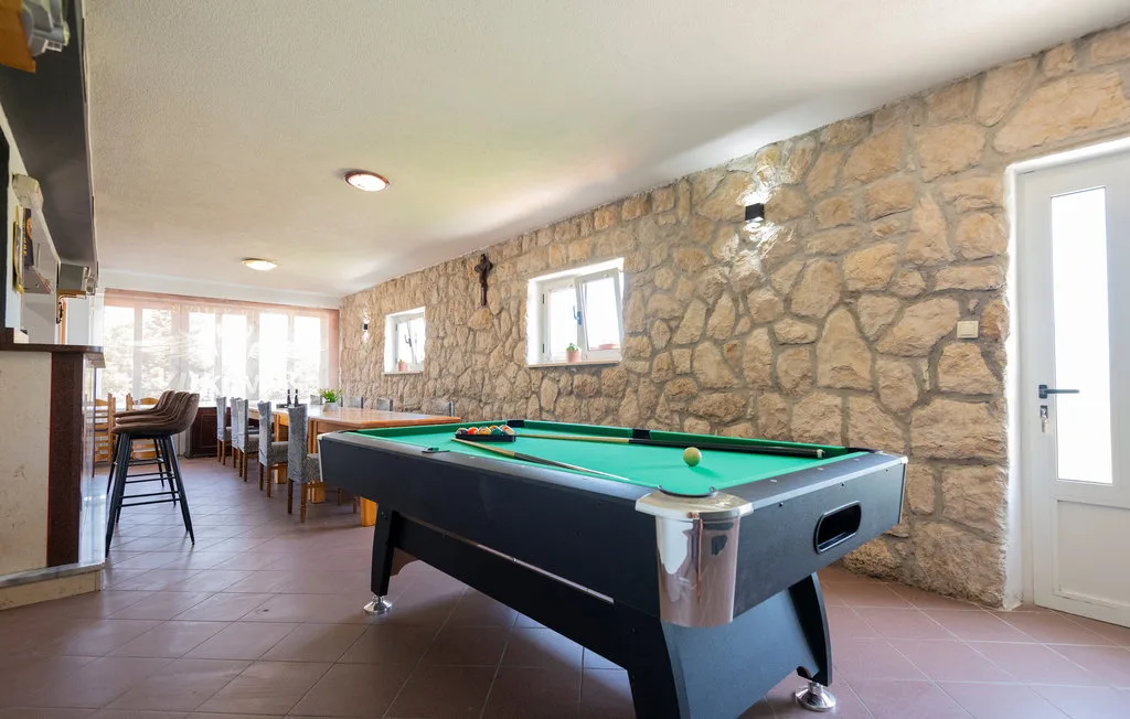 Una mesa de billar está en una sala de juegos con paredes de piedra y mesas de comedor al lado.
