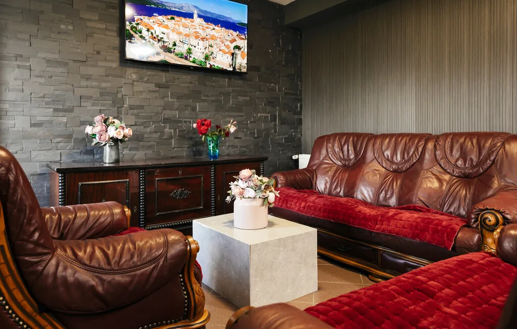 Una sala de estar con asientos de cuero marrón, cojines rojos y un televisor en la pared.