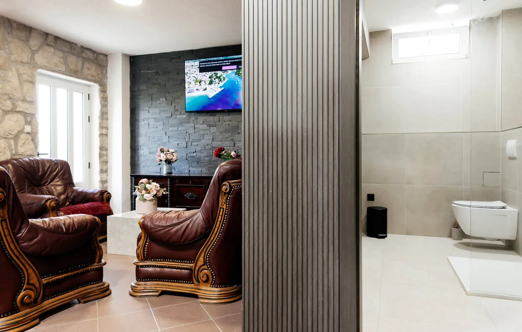 Una sala de estar con asientos ornamentados y un televisor en la pared junto a un baño con azulejos.