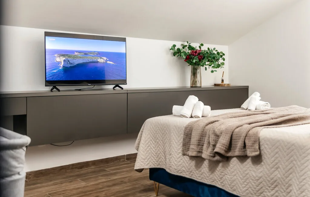 Un dormitorio con un televisor sobre un mueble largo y oscuro y camas con ropa de cama clara.