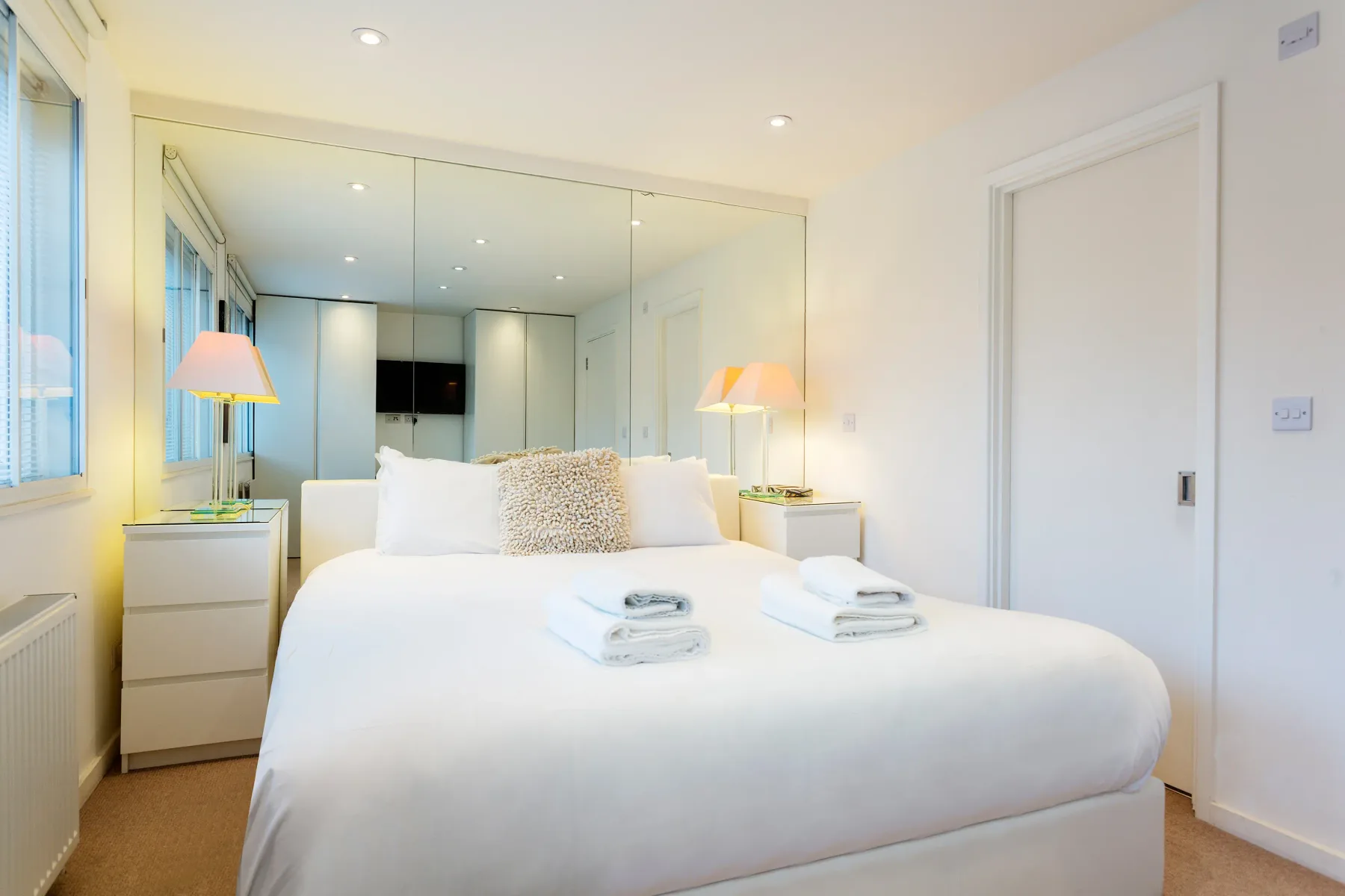 Un dormitorio luminoso con una cama bien hecha y una pared con espejos.