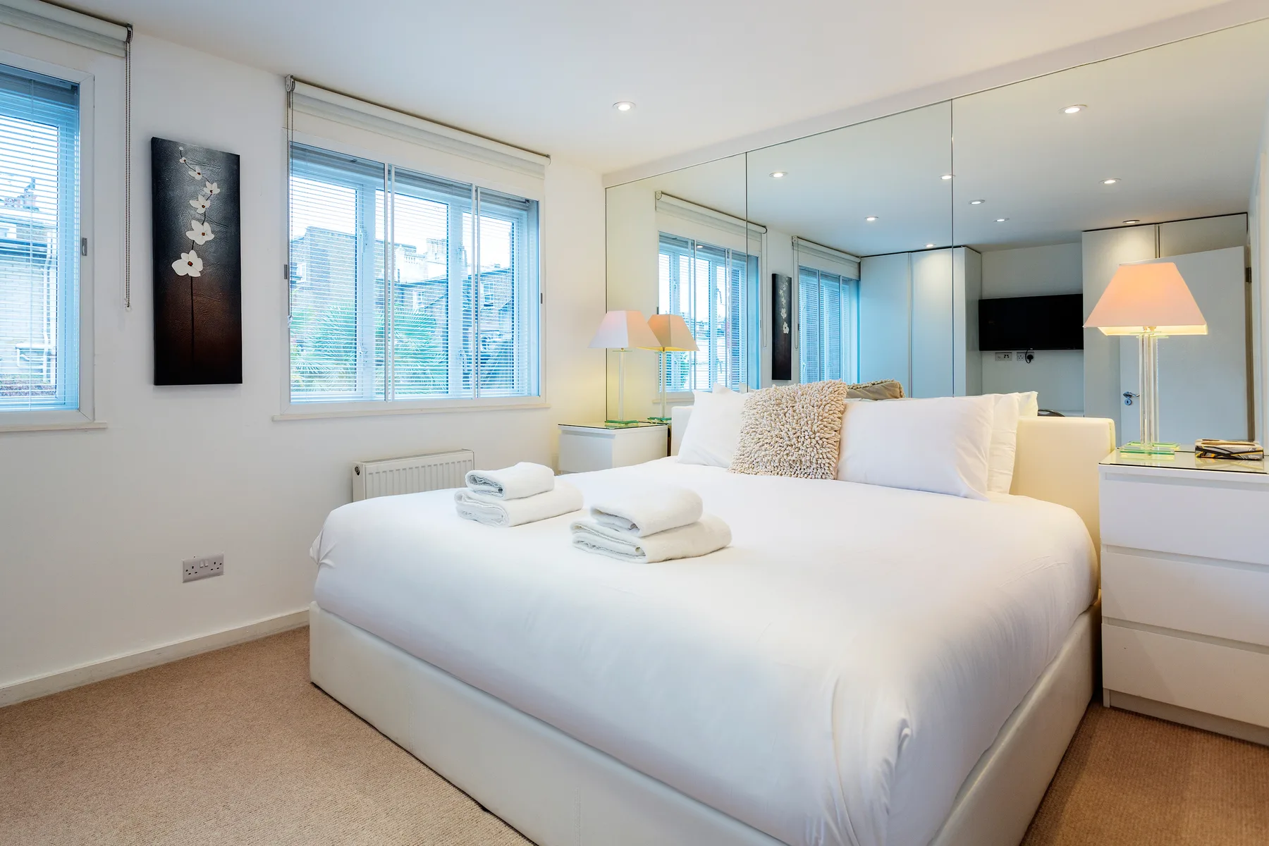 Un dormitorio luminoso con una cama bien tendida y una pared con espejos.