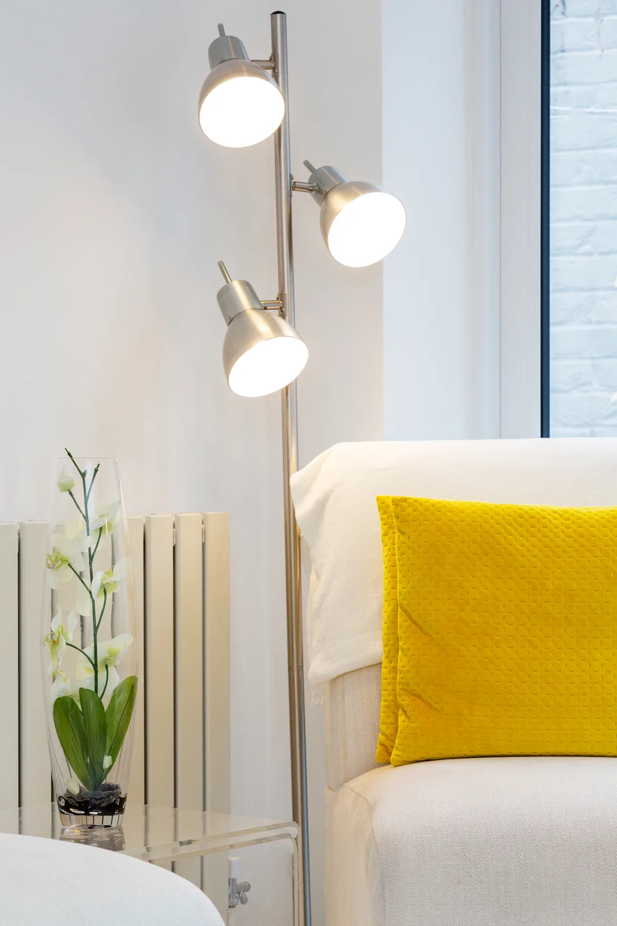 Una luminosa zona de estar con asiento blanco, un cojín amarillo y una lámpara de pie.