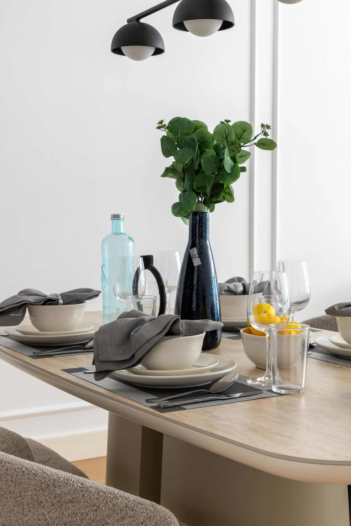Una mesa de comedor está preparada con platos, vasos y un centro de mesa frondoso.