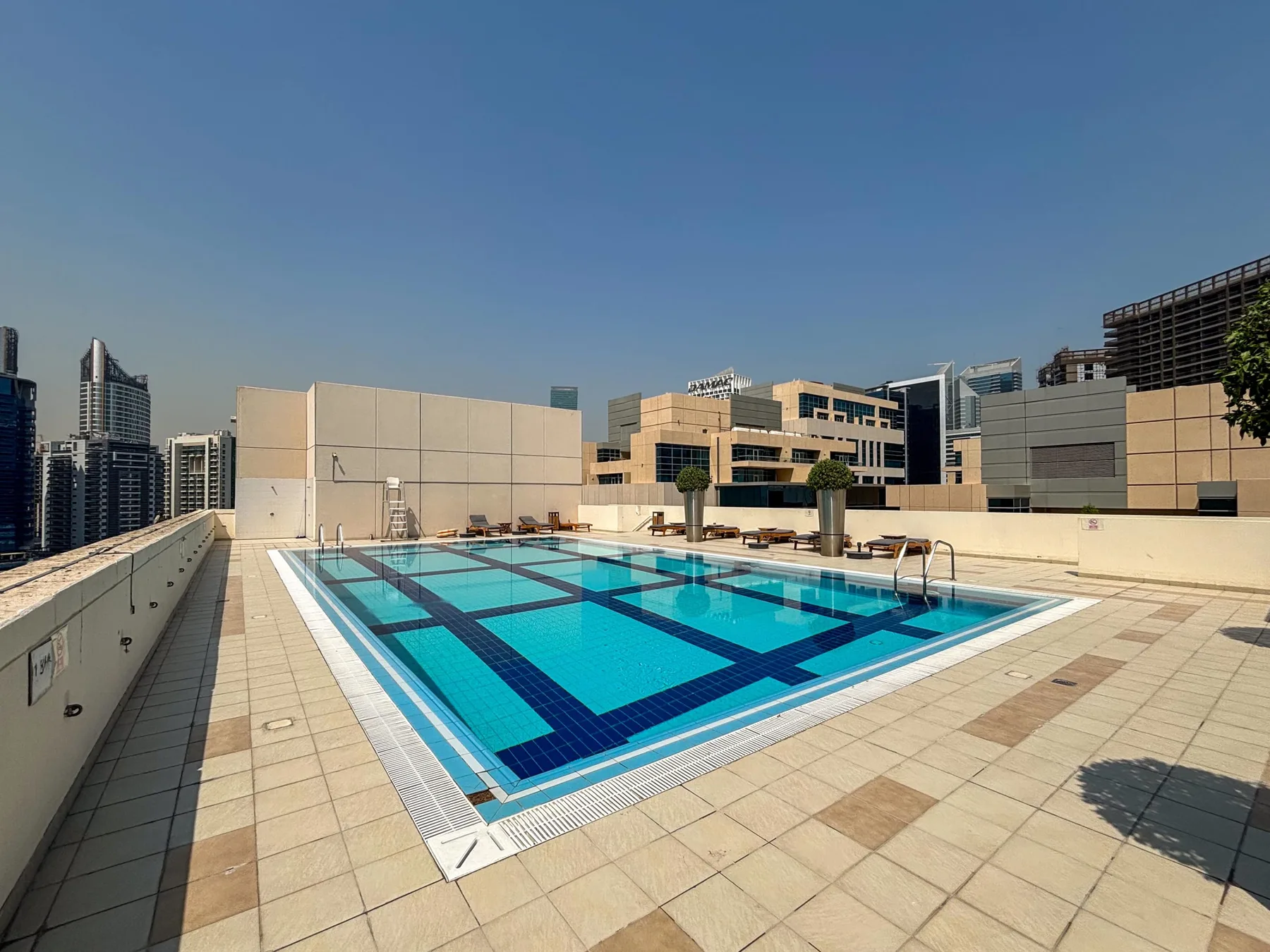 Una piscina en la azotea ocupa una terraza embaldosada entre edificios de la ciudad.