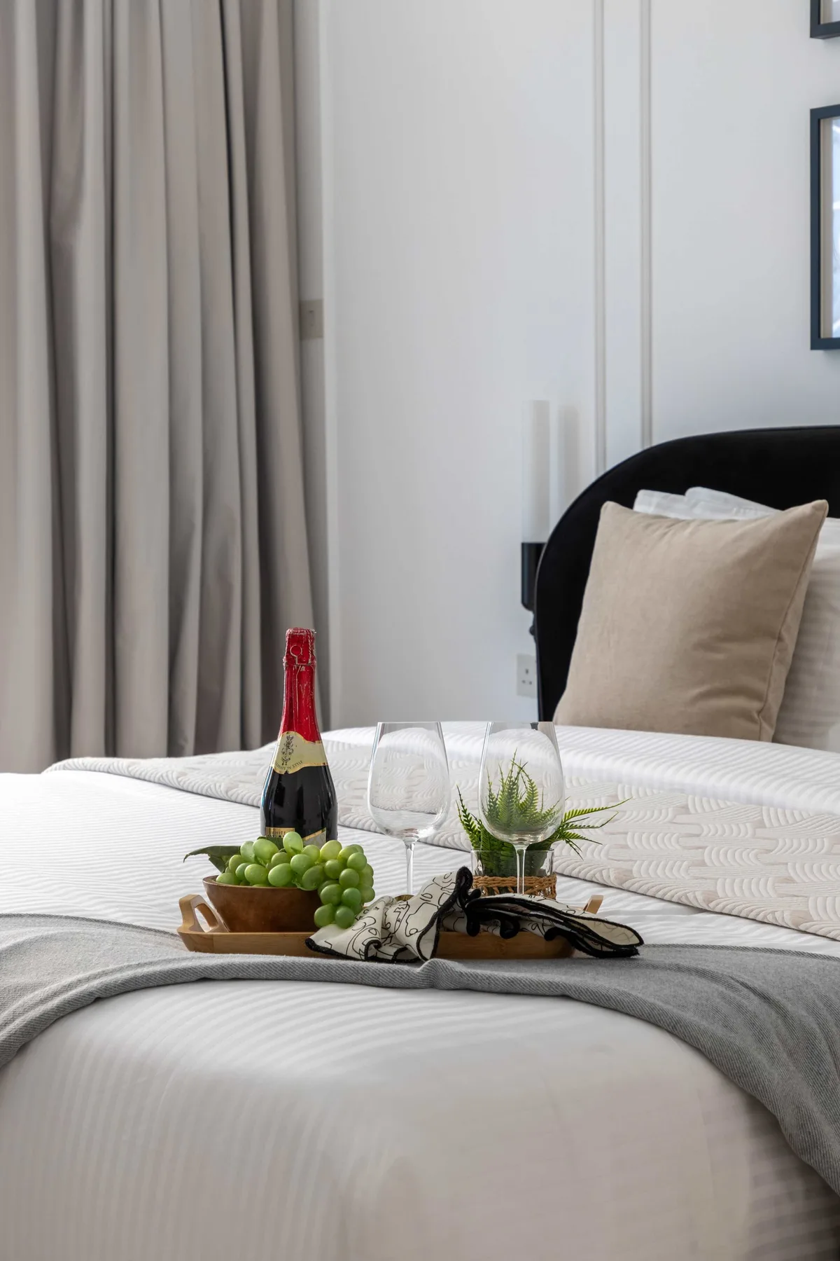 Un dormitorio con una cama bien arreglada, bebidas y cortinas.