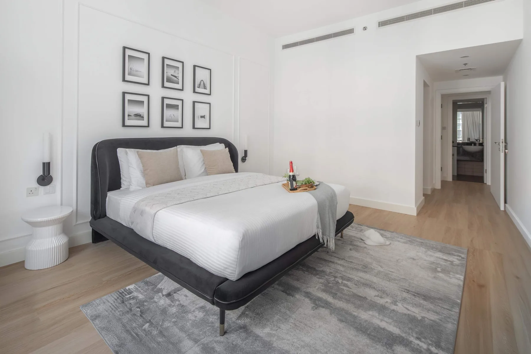 Un dormitorio con una cama bien hecha, cuadros enmarcados y una alfombra gris.