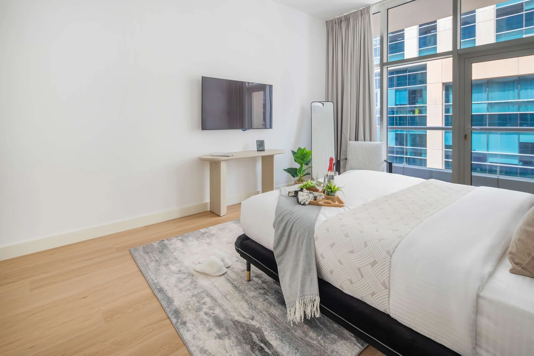 Un dormitorio luminoso con una cama junto a grandes ventanales con edificios cercanos a la vista.