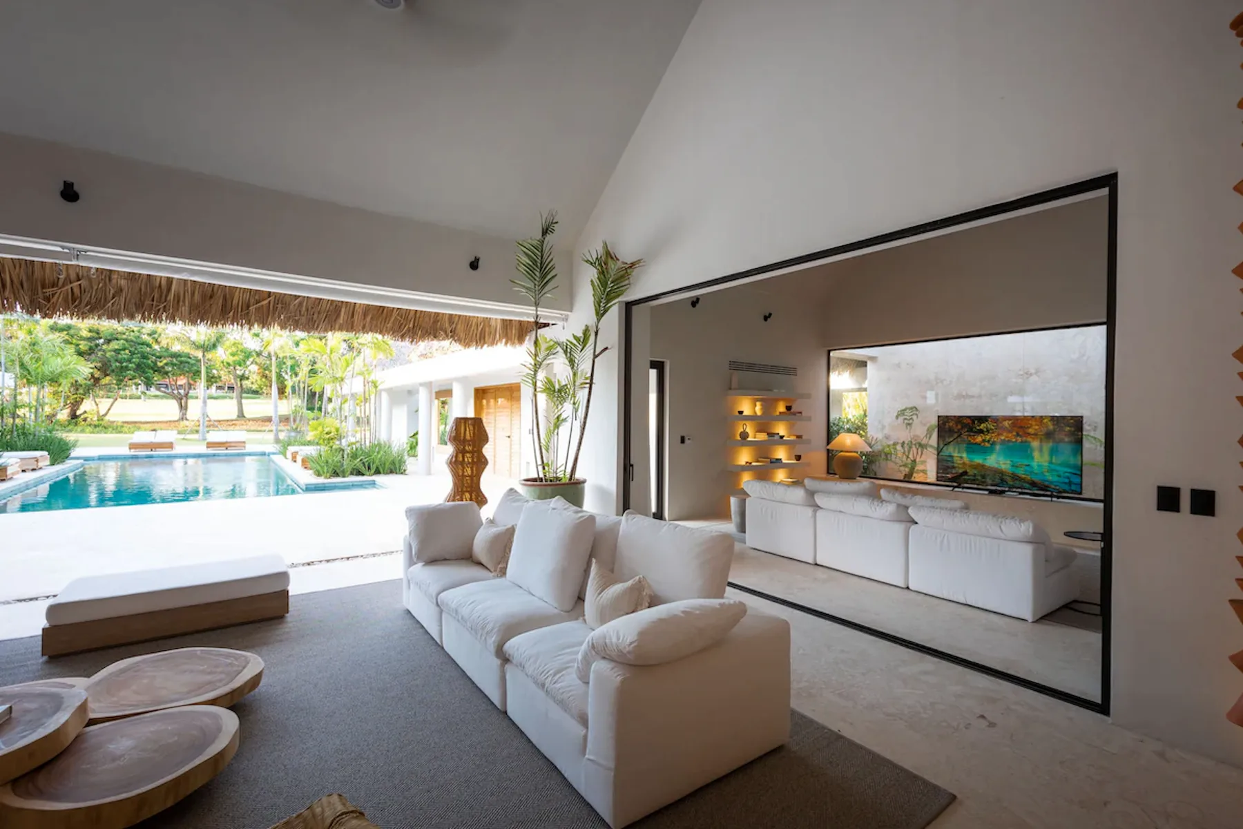 A bright living room opens onto a covered patio beside a swimming pool.