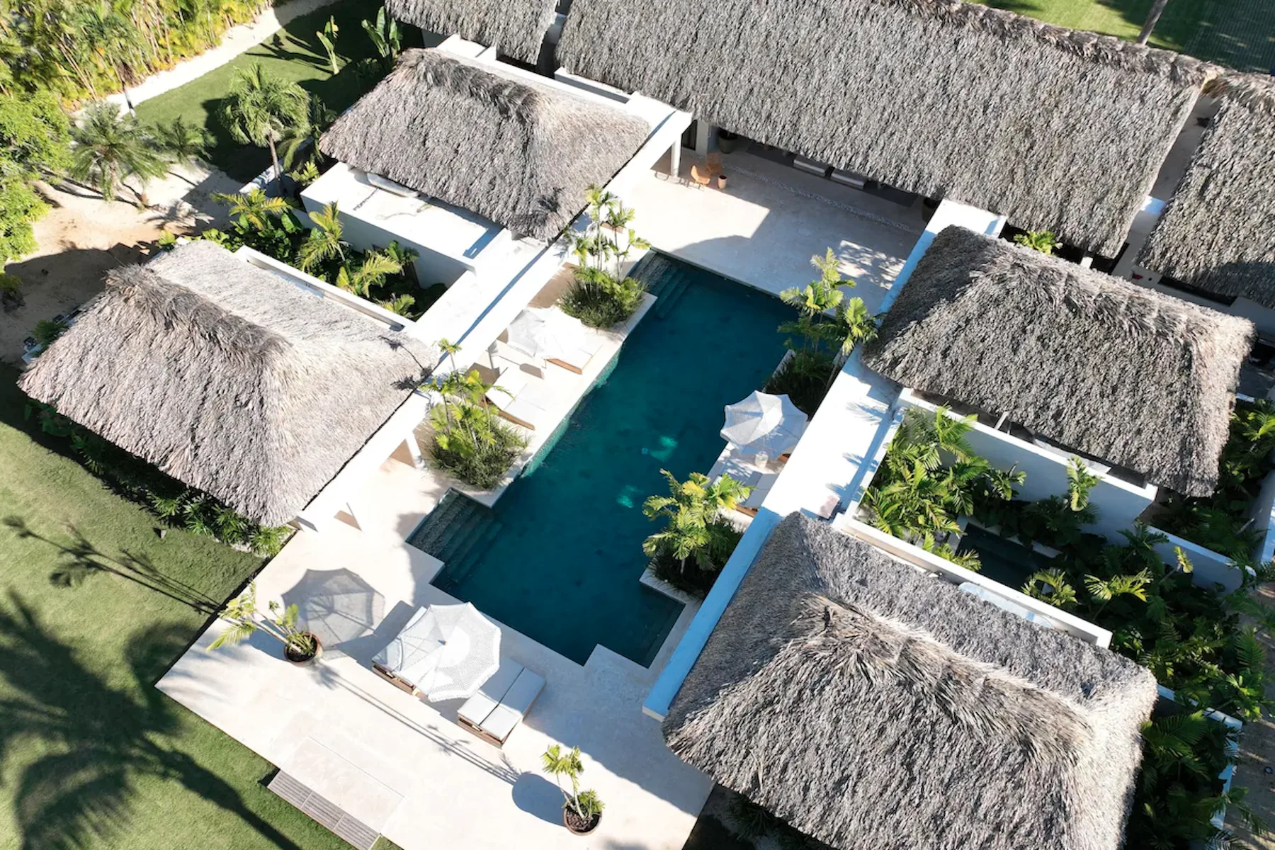 An aerial view of a swimming pool surrounded by thatched-roof buildings and greenery.