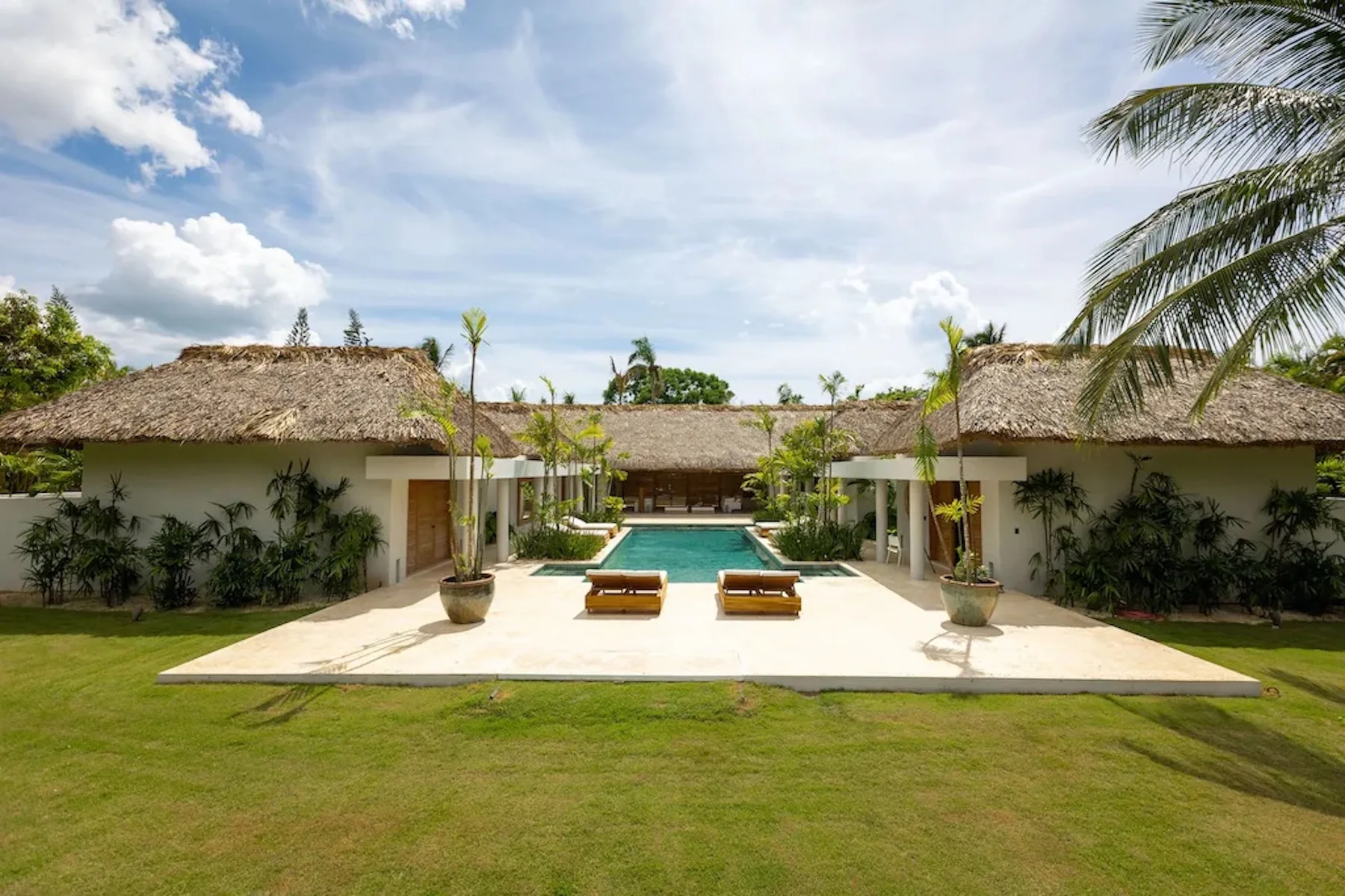 A landscaped courtyard with a swimming pool, lounge chairs, and thatched-roof buildings.