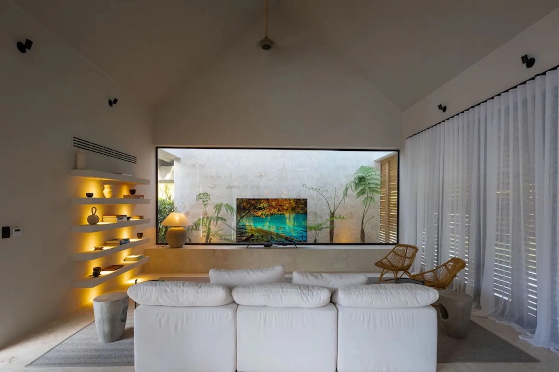 A living room with white seating facing a television and a wide window.