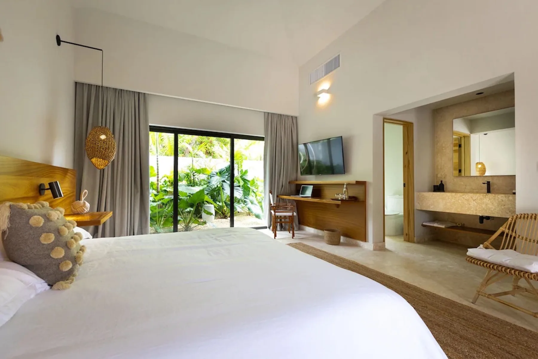 A bright bedroom with a large bed, sliding glass doors, and greenery outside.