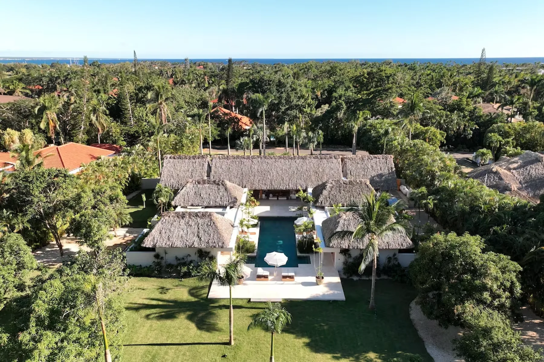 Aerial view of a tropical resort with thatched-roof buildings and a central pool.