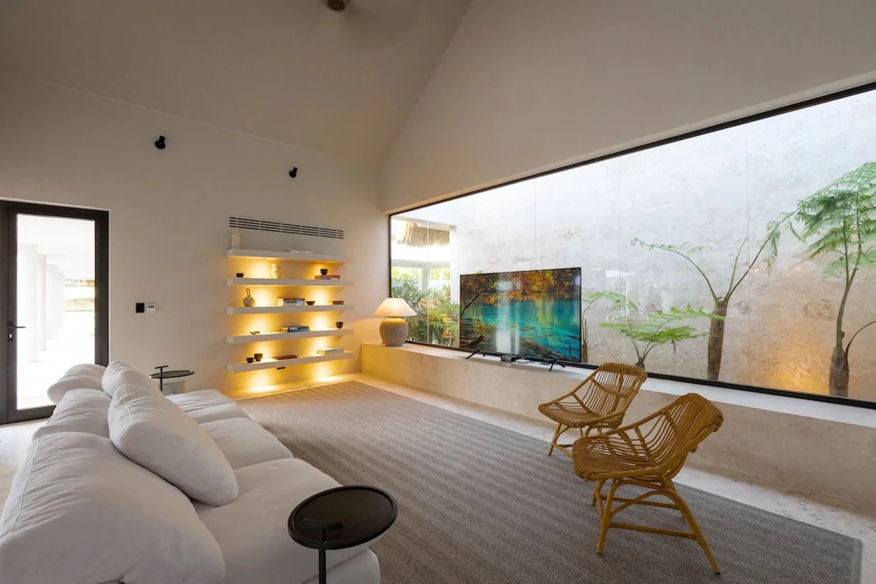 A modern living room with a large window, seating, and illuminated wall shelves.