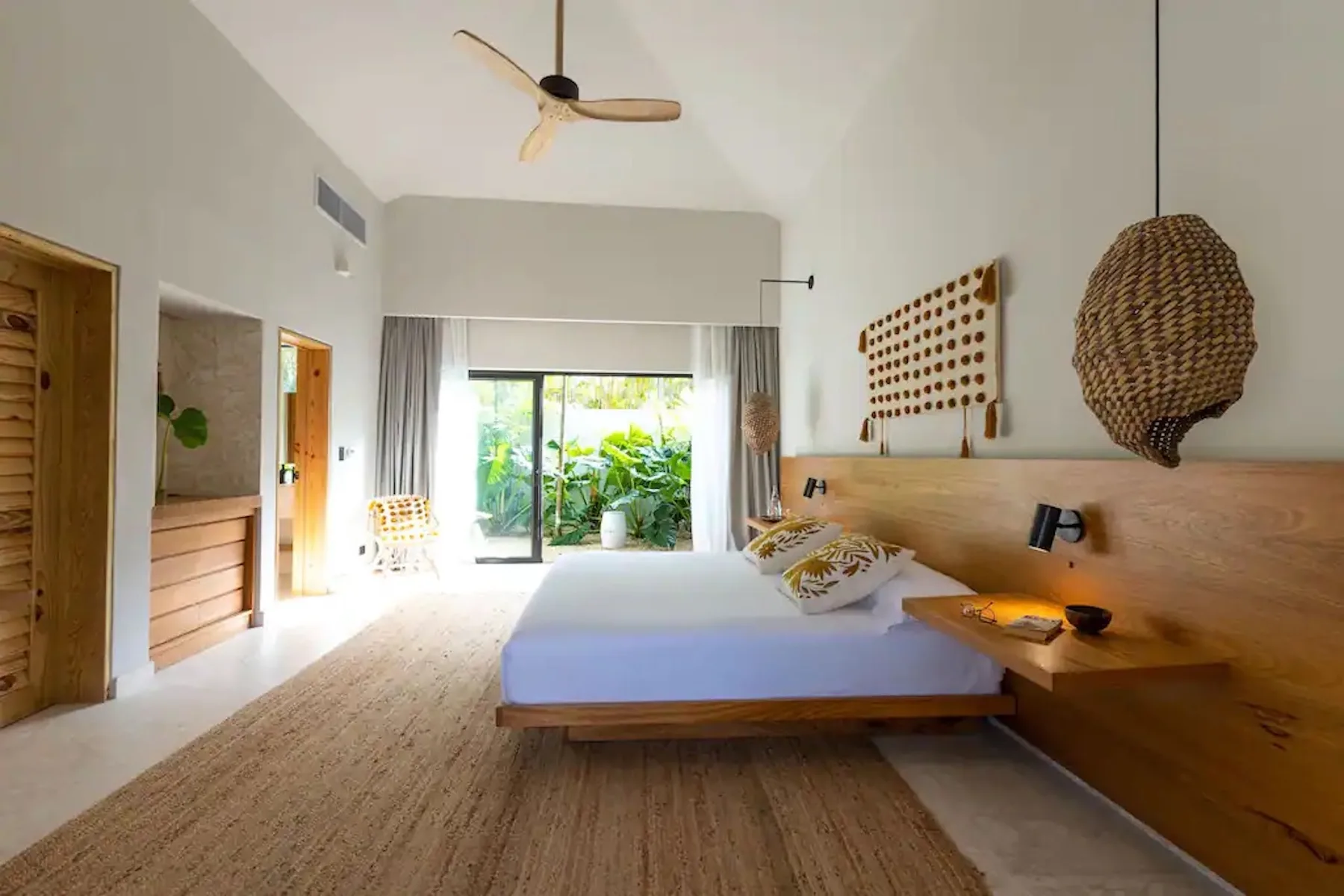 A bright bedroom with a low bed and sliding glass doors opening to greenery.