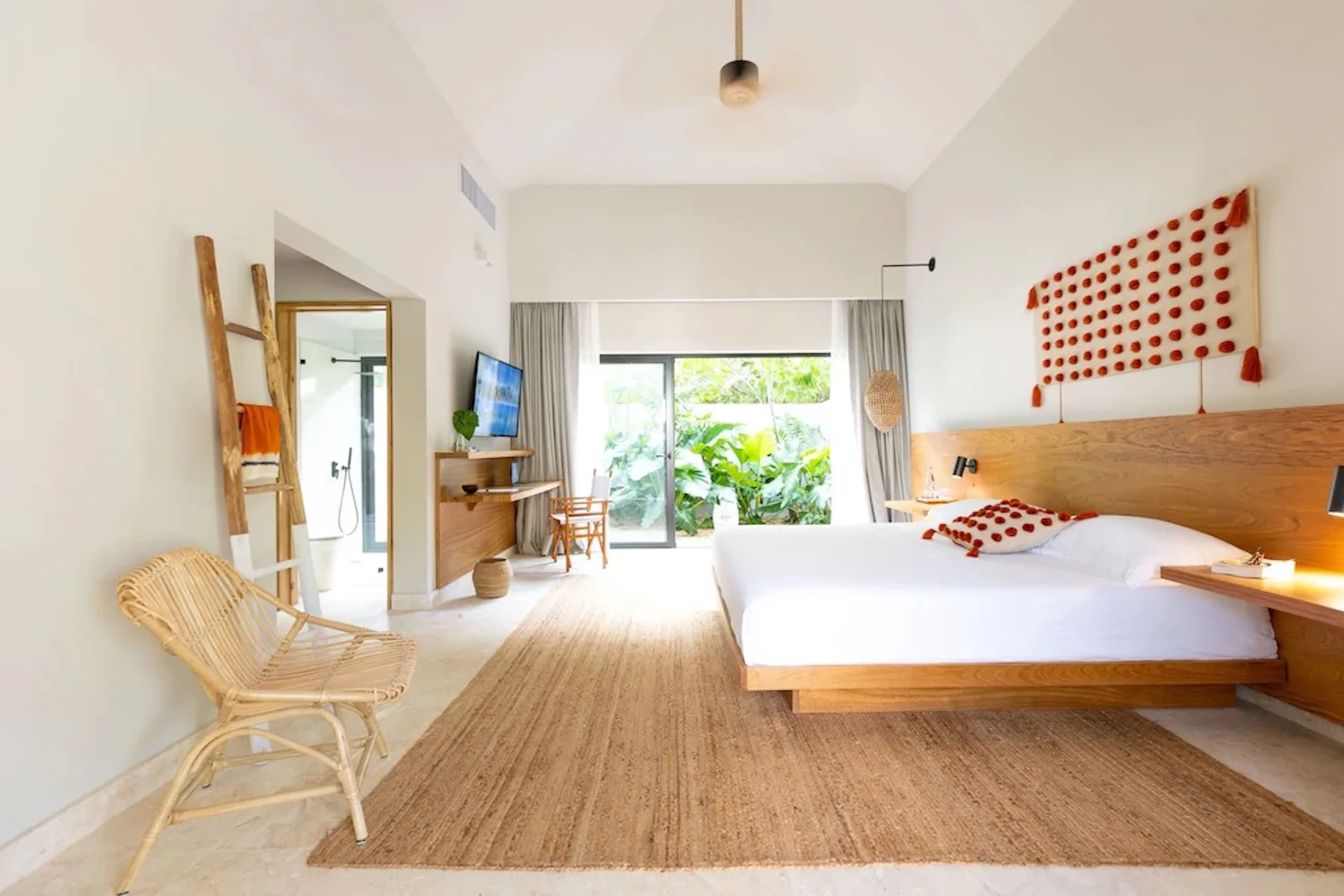 A bright bedroom with a wooden bed, bedside table, and glass doors opening to greenery.