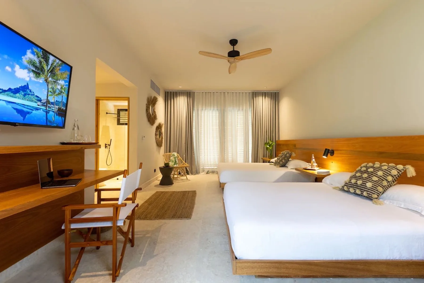 A bright bedroom with a large bed, curtained windows, and a desk area.