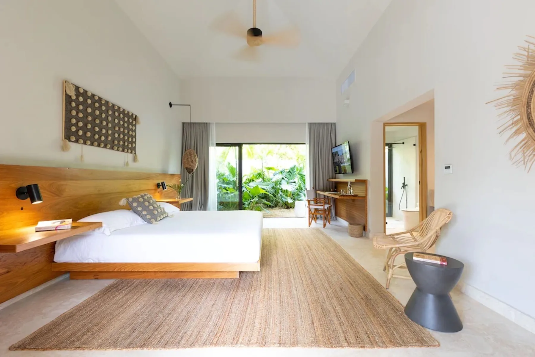 A bright bedroom with a bed, woven rug, and sliding glass doors opening to greenery.